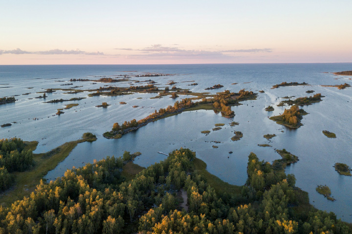 Photograph taken at sunset of tiny islands in the Kvarken Archipelago. Open ocean extends to the‌ horizon.