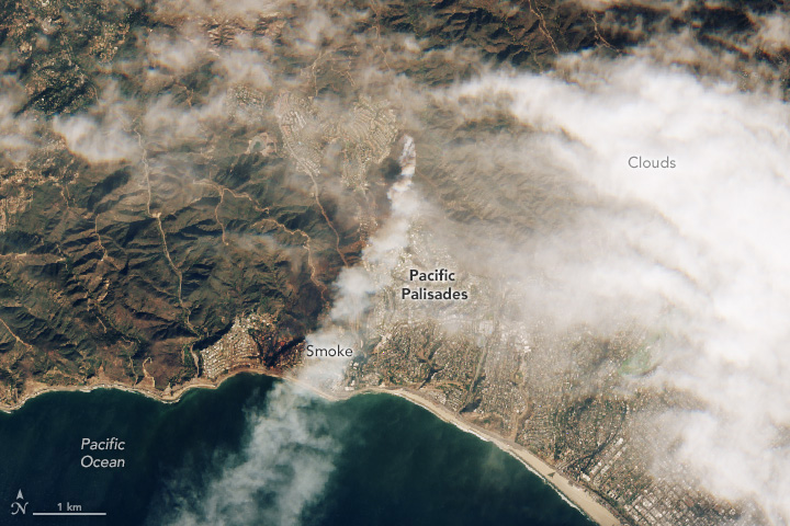 A satellite image of the Pacific Palisades in coastal Southern California. Smoke can be seen streaming from a fire, out toward the Pacific Ocean.