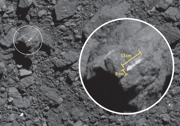 An image captured by the OSIRIS-REx spacecraft shows a boulder on the surface of the asteroid Bennu. The boulder is mostly dark except for a bright vein of a carbonate mineral visible on one side of it. The vein is about 8 centimeters wide and 53 centimeters long.